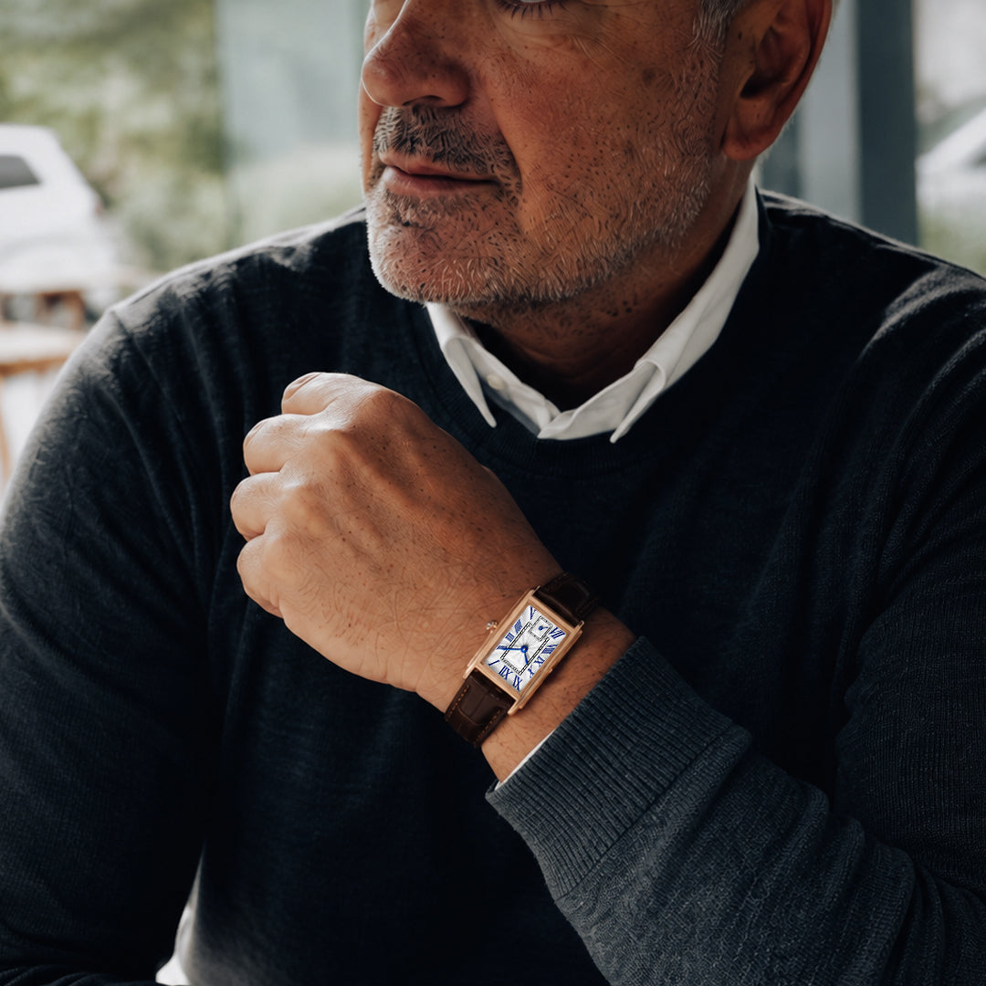 The 1927 gold tank watch on a man's wrist, silver dial with blue Roman numerals, navy sweater
