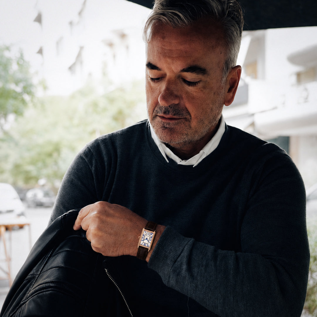 A distinguished man wearing the 1927 gold tank watch with brown leather strap at an outdoor cafe
