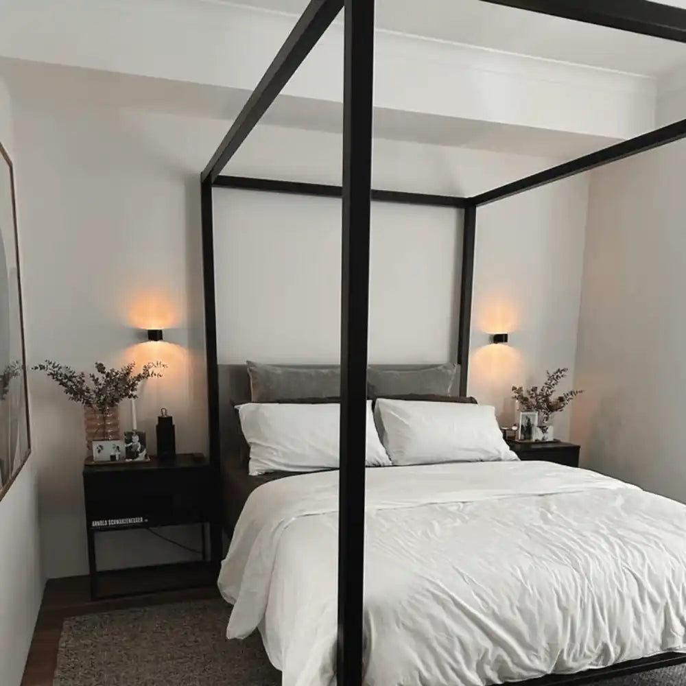 LED rechargeable wall sconce — pair installed either side of a four-poster black bed, lighting the nightstands